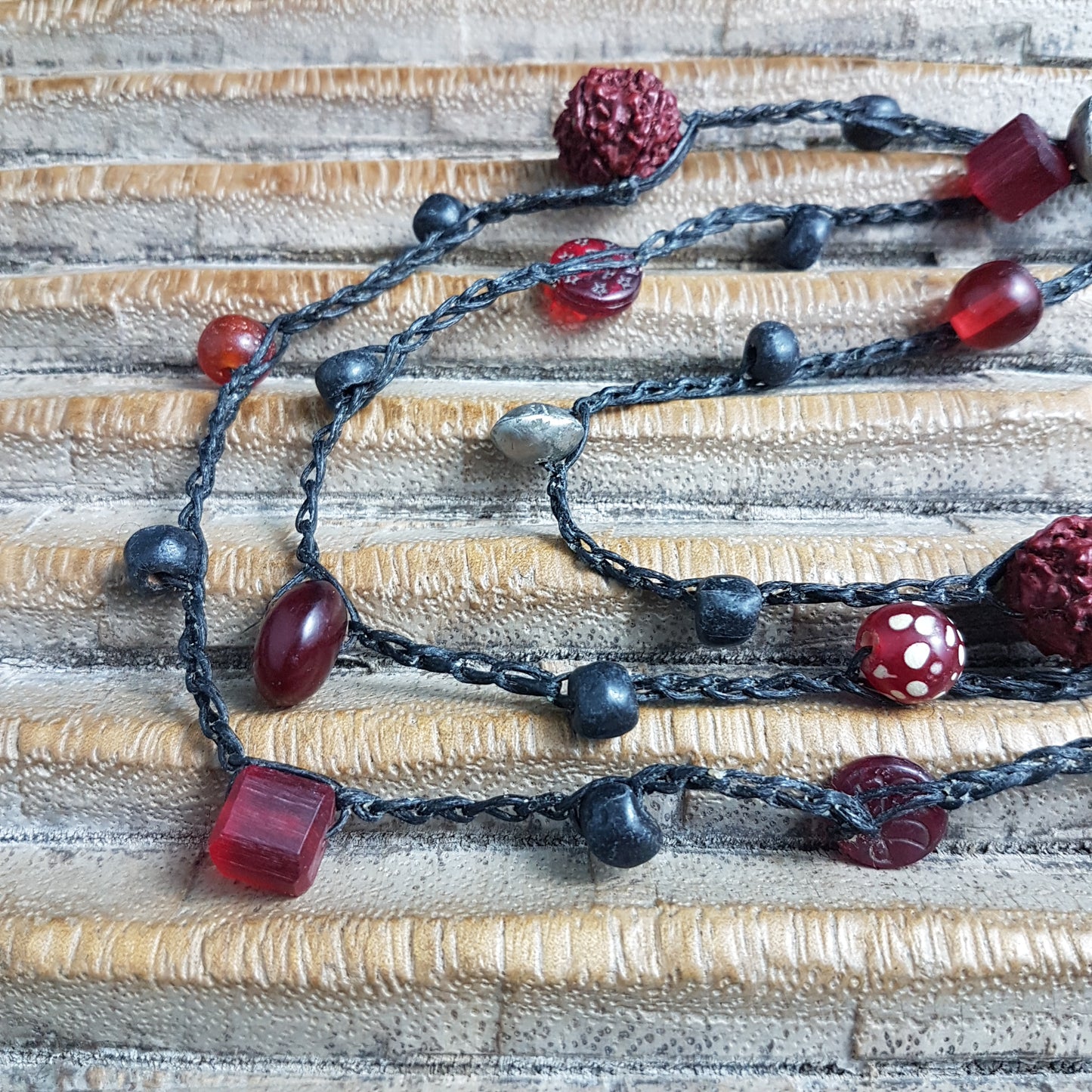 Lange handgehäkelte Kette mit Rudraksha-Samen aus nepalesischen Gebets-Malas, schwarzen indonesischen Wickelglasperlen, Harzperlen in Rottönen und roten Glasperlen von der Insel Java auf Baumwolle