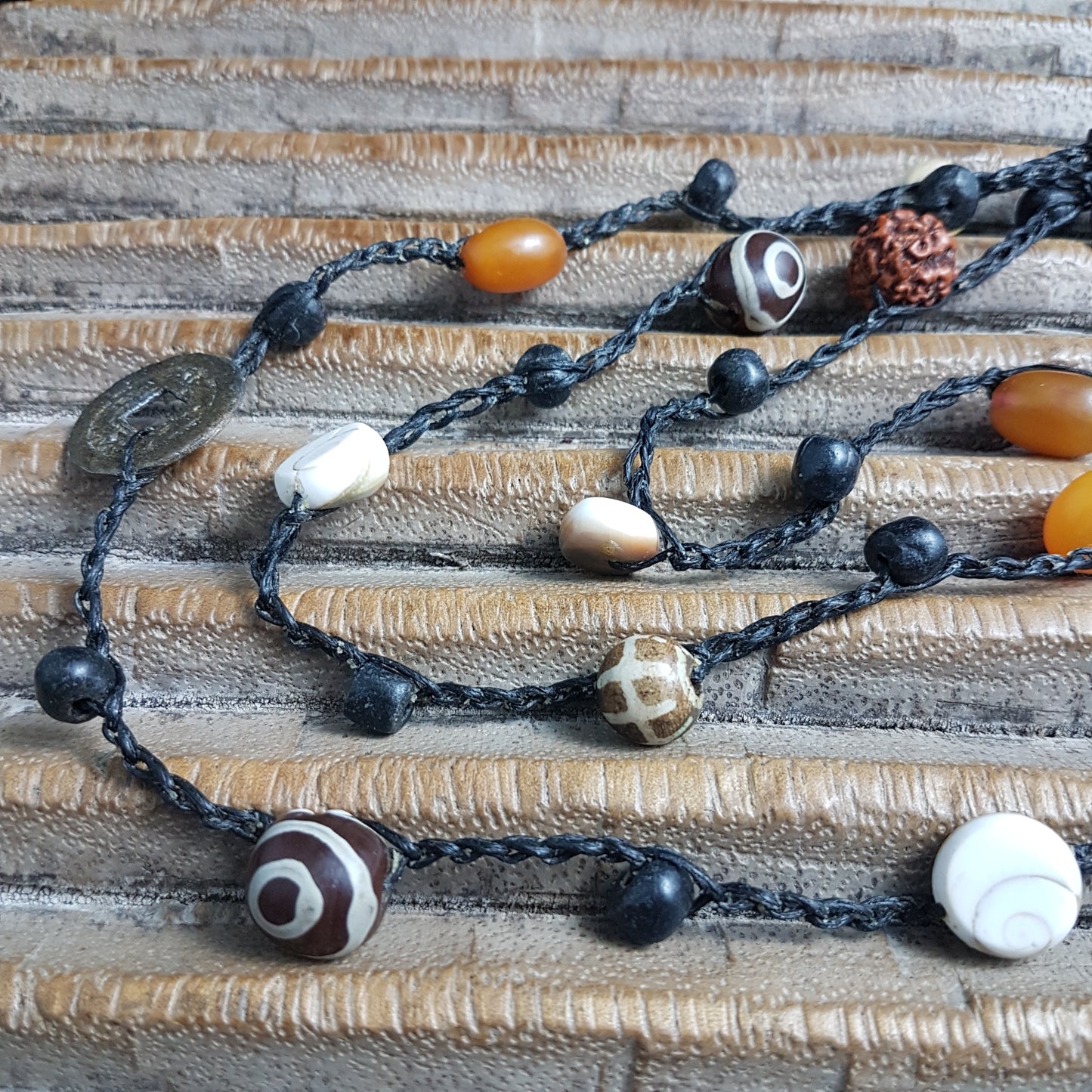 Lange handgehäkelte Kette mit Rudraksha-Samen aus nepalesischen Gebets-Malas, schwarzen indonesischen Wickelglasperlen, braunen und gelben Harzperlen, weißen Shiva-Muscheln und gestreiften Perlen aus versteinertem Holz aus Burma auf Baumwolle
