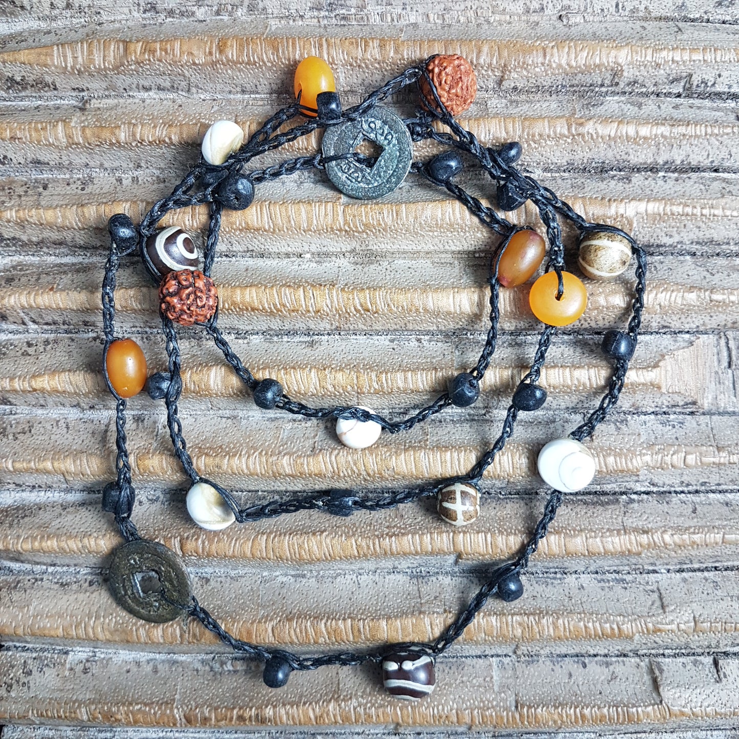 Lange handgehäkelte Kette mit Rudraksha-Samen aus nepalesischen Gebets-Malas, schwarzen indonesischen Wickelglasperlen, braunen und gelben Harzperlen, weißen Shiva-Muscheln und gestreiften Perlen aus versteinertem Holz aus Burma auf Baumwolle