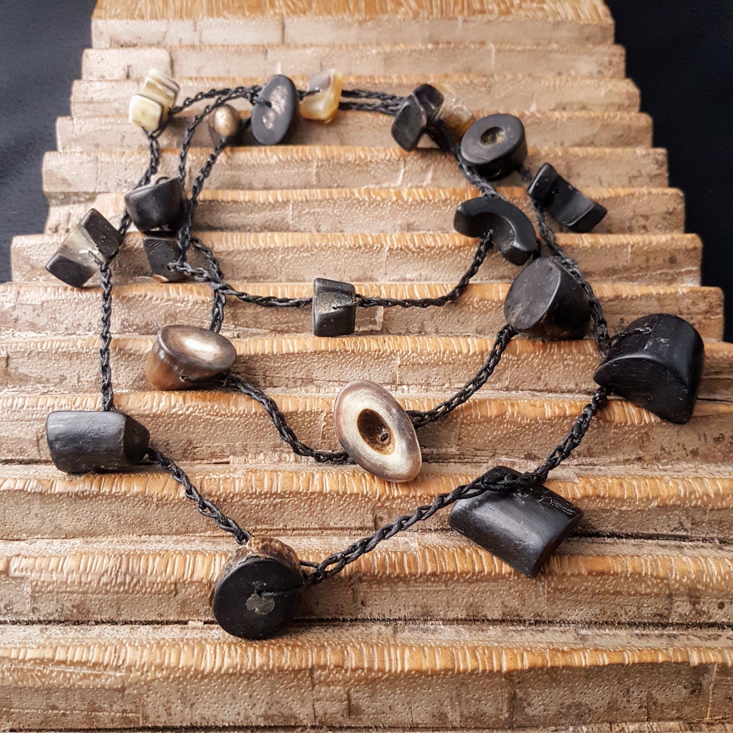 Lange handgehäkelte Kette mit Hornperlen in verschiedenen Formen auf Baumwolle