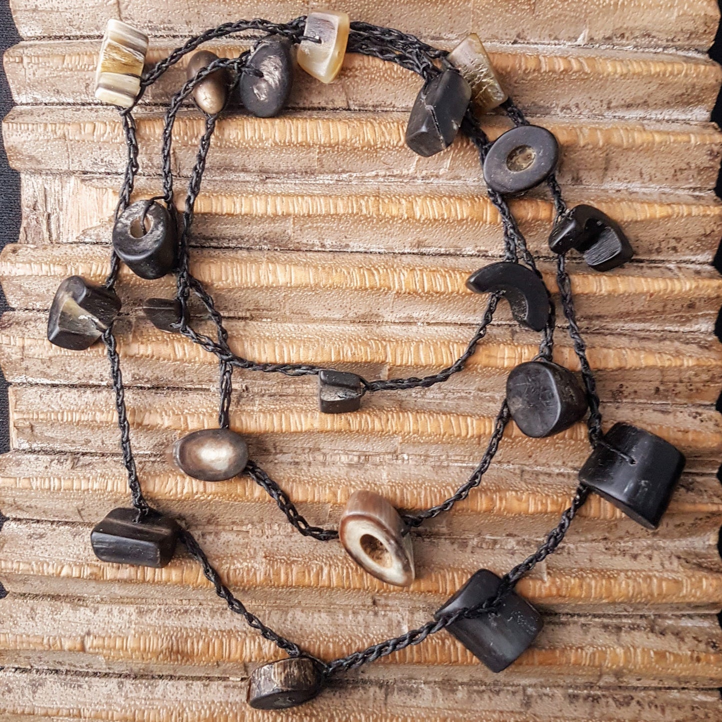 Lange handgehäkelte Kette mit Hornperlen in verschiedenen Formen auf Baumwolle