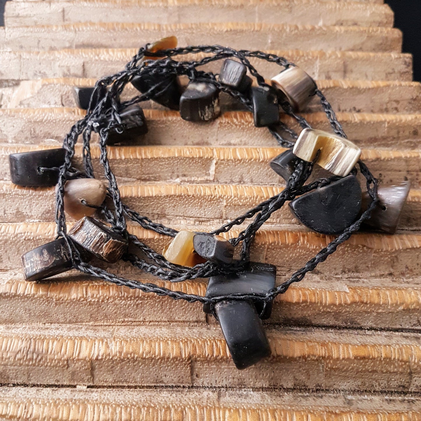 Lange handgehäkelte Kette mit Hornperlen in verschiedenen Formen auf Baumwolle