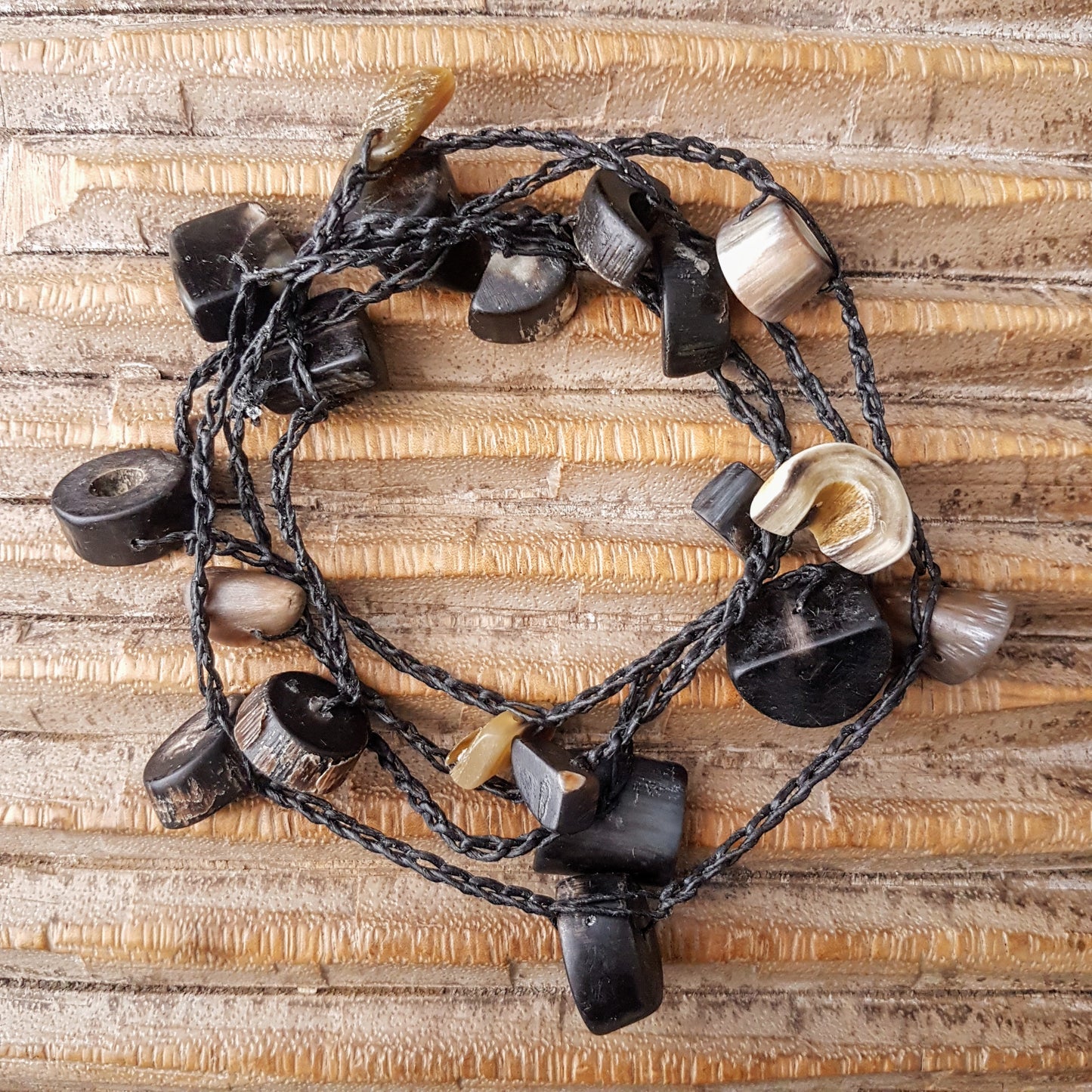 Lange handgehäkelte Kette mit Hornperlen in verschiedenen Formen auf Baumwolle