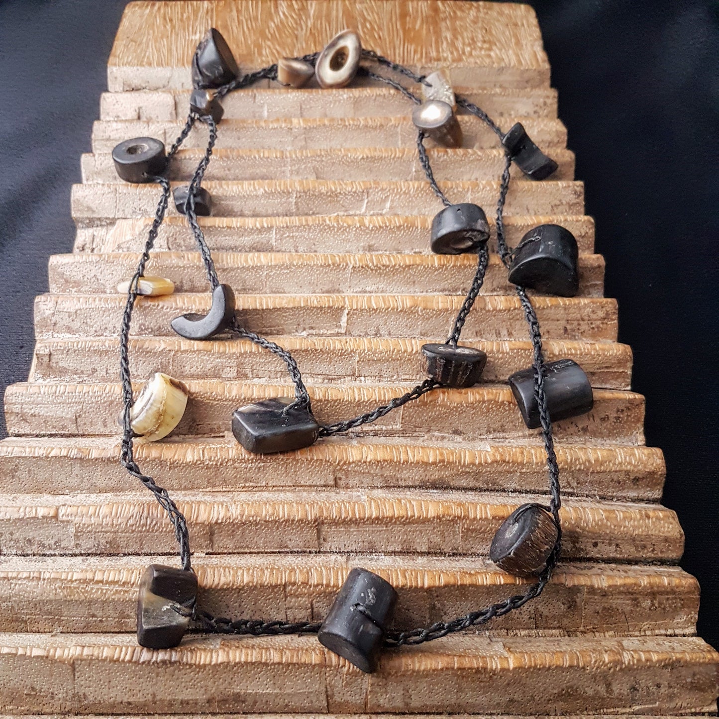 Lange handgehäkelte Kette mit Hornperlen in verschiedenen Formen auf Baumwolle