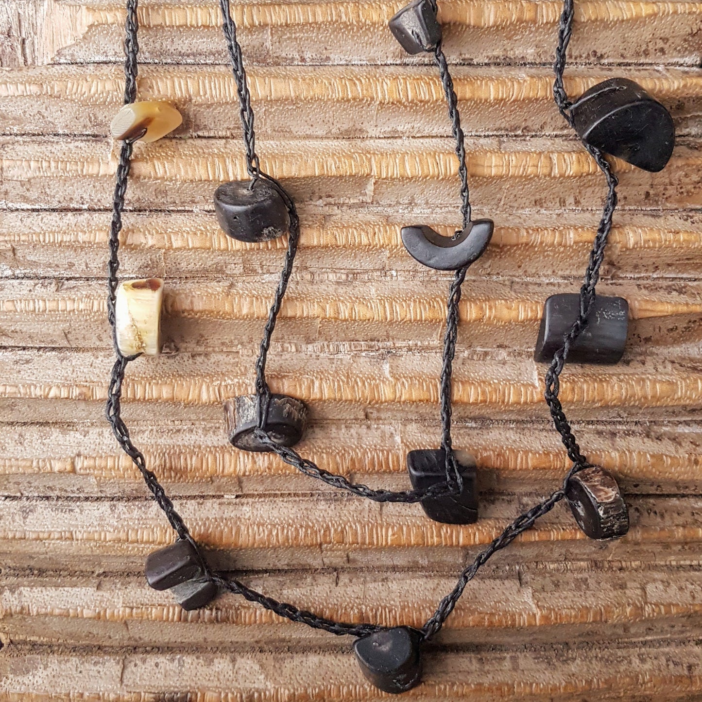 Lange handgehäkelte Kette mit Hornperlen in verschiedenen Formen auf Baumwolle