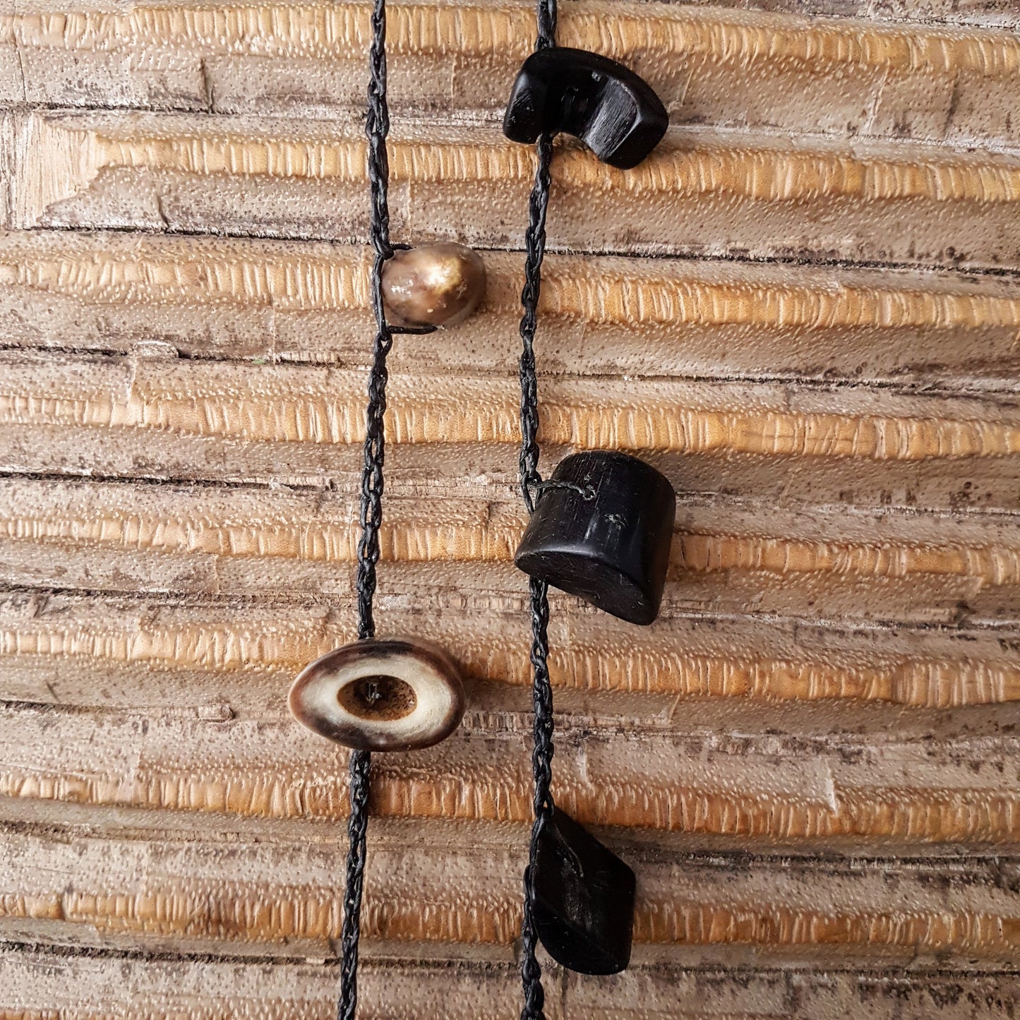Lange handgehäkelte Kette mit Hornperlen in verschiedenen Formen auf Baumwolle