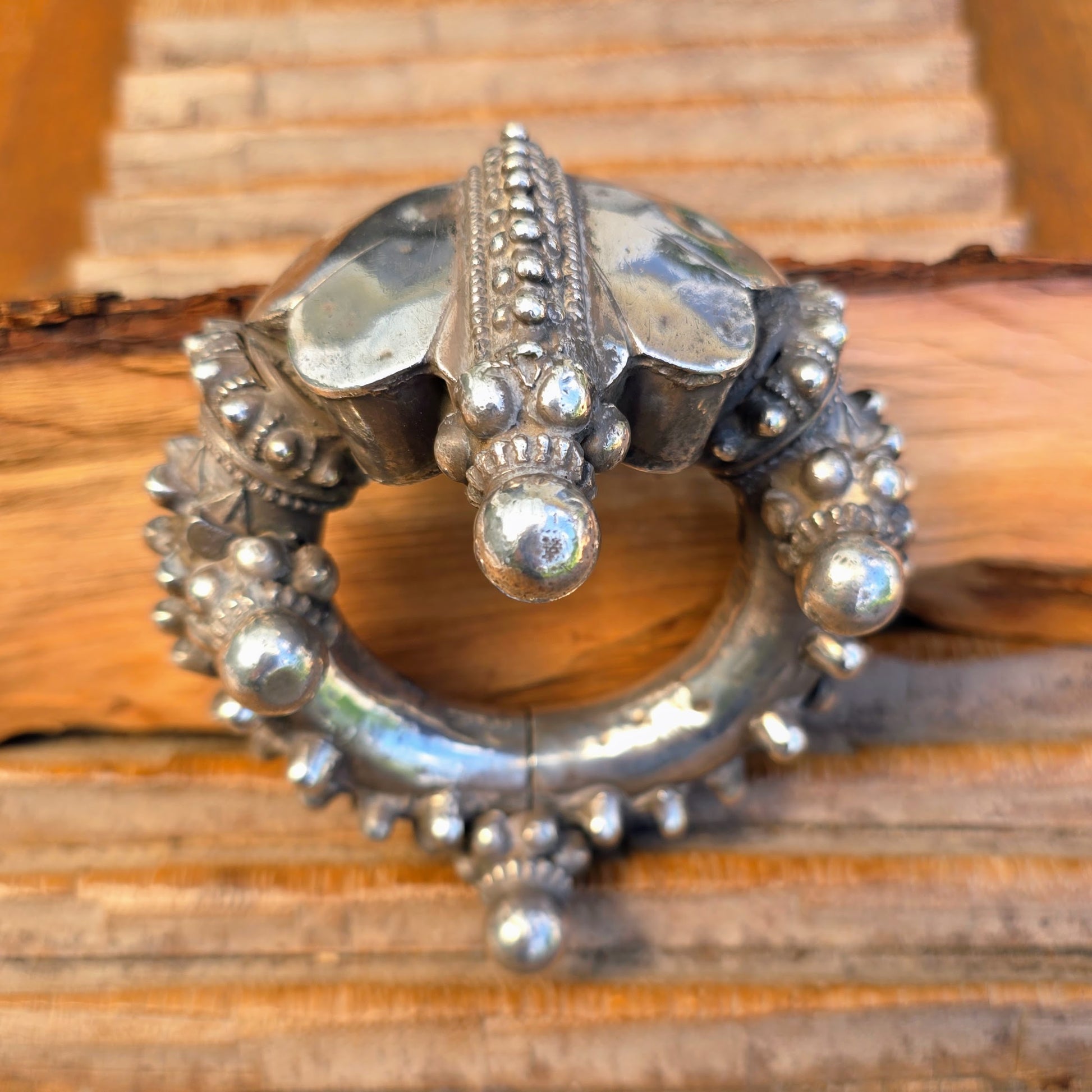 Silberarmreif zum Aufklappen – Rajasthan, Indien | Antik | Handgearbeitet
Ein charakterstarkes Einzelstück aus Rajasthan: Dieser massive, handgeschmiedete Silberarmreif lässt sich seitlich aufklappen und wird traditionell von Kunsthandwerkerinnen und -handwerkern in aufwendiger Repoussé- und Granulationsarbeit gefertigt. Die plastischen Kugel- und Blütenelemente sowie feine Punktreihen verleihen dem Schmuckstück eine skulpturale Präsenz – roh, sinnlich, authentisch. 